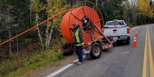 Technician feeding underground cable from reel trailer during roadside utility installation